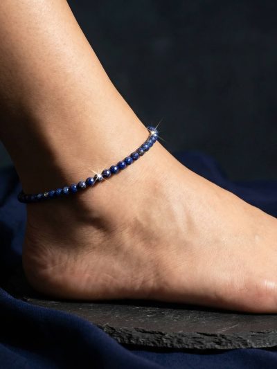 Lapis lazuli anklet worn on ankle on dark navy linen in cool morning light