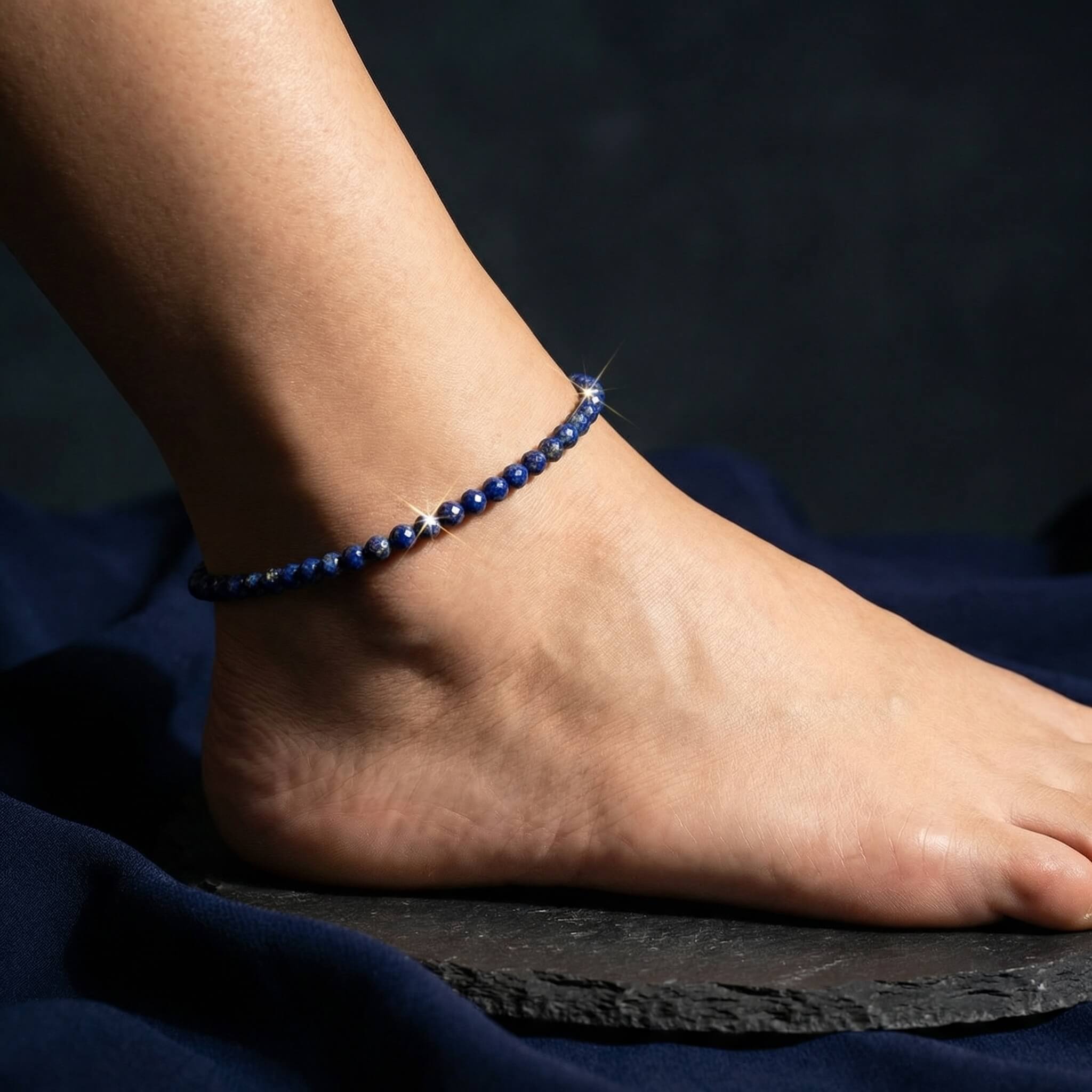 Lapis lazuli anklet worn on ankle on dark navy linen in cool morning light