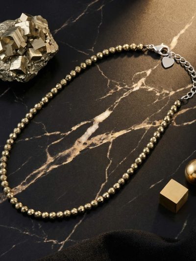 Sunavyaa pyrite crystal anklet flat lay on black marble with raw pyrite cube and golden flower