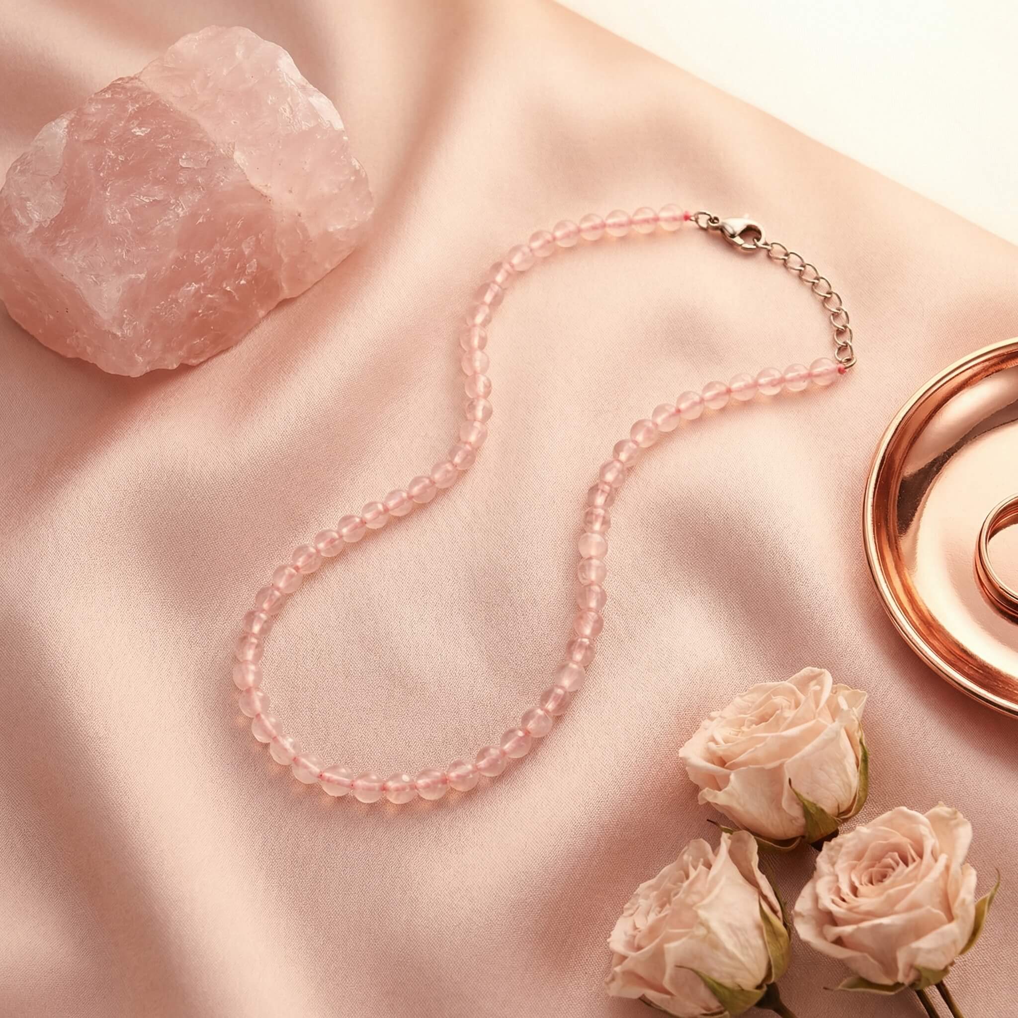 Sunavyaa rose quartz crystal anklet flat lay on ivory silk with pink rose petals and tumbled stone